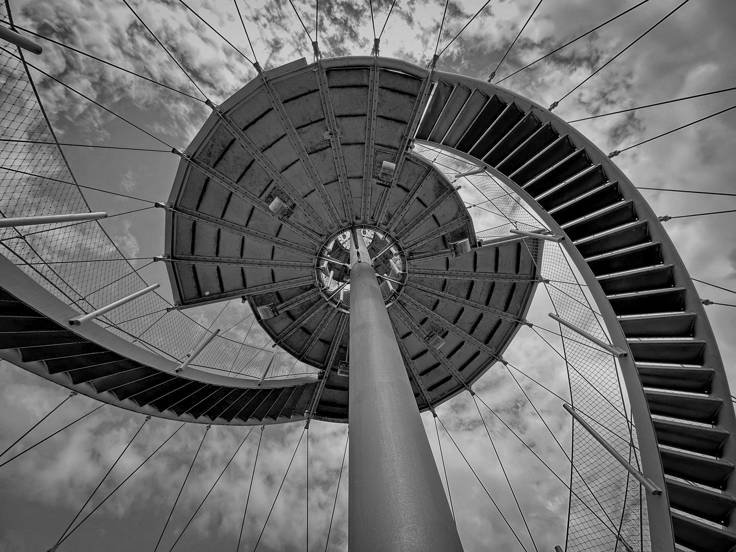 Escalera de caracol metálica que asciende en espiral hacia el cielo, simbolizando el camino ascendente y estratégico hacia el éxito y el posicionamiento en el mercado.